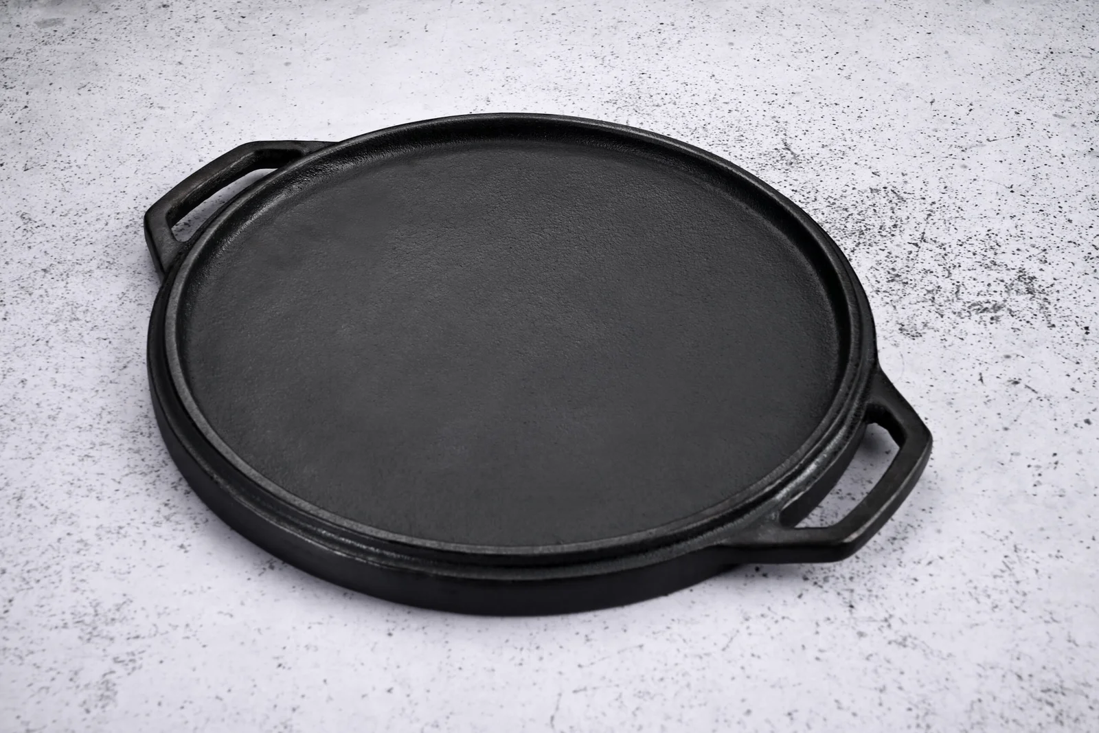 Smooth flat side of a 30 cm heavy-duty dual-sided cast iron round griddle with two loop handles
